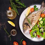 Pesce al forno con limone fresco insalata piatto bianco scuro rustico sfondo vista dall'alto cena sana con ristorante di pesce rogoznica