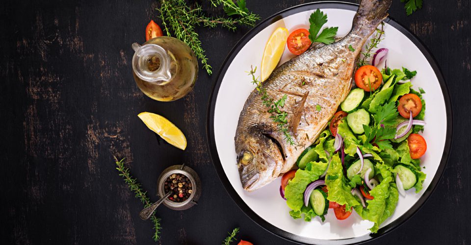 Baked fish with lemon fresh salad white plate dark rustic background top view healthy dinner with fish restaurant rogoznica