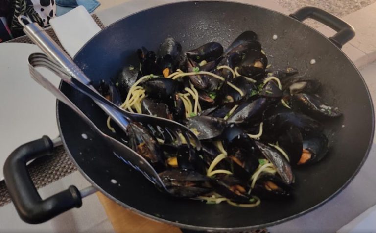 mussels on the table in a black bowl with pasta